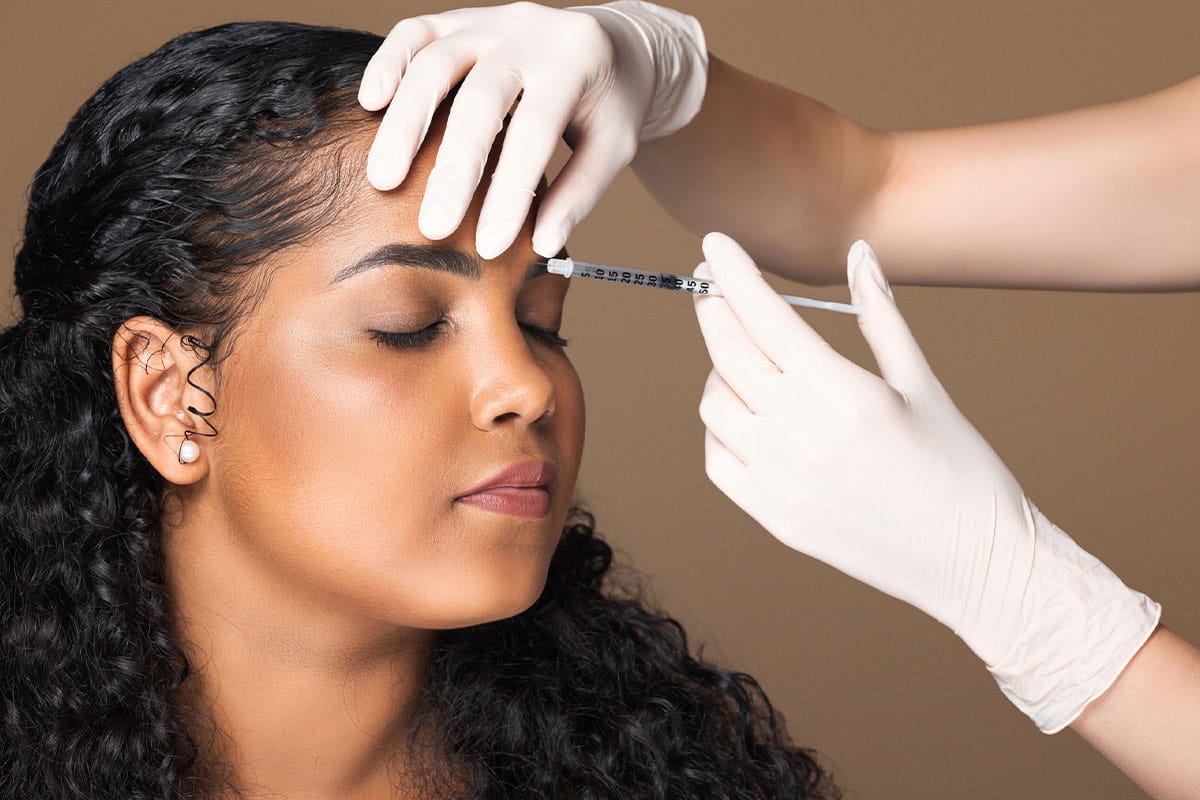 Woman receiving cosmetic forehead injection from gloved professional.