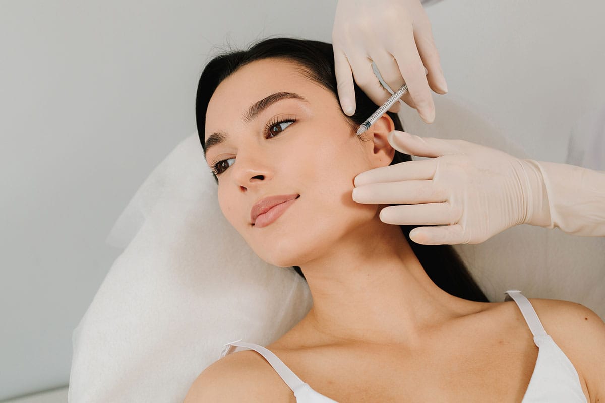 Woman receiving cosmetic injection near ear from gloved professional.