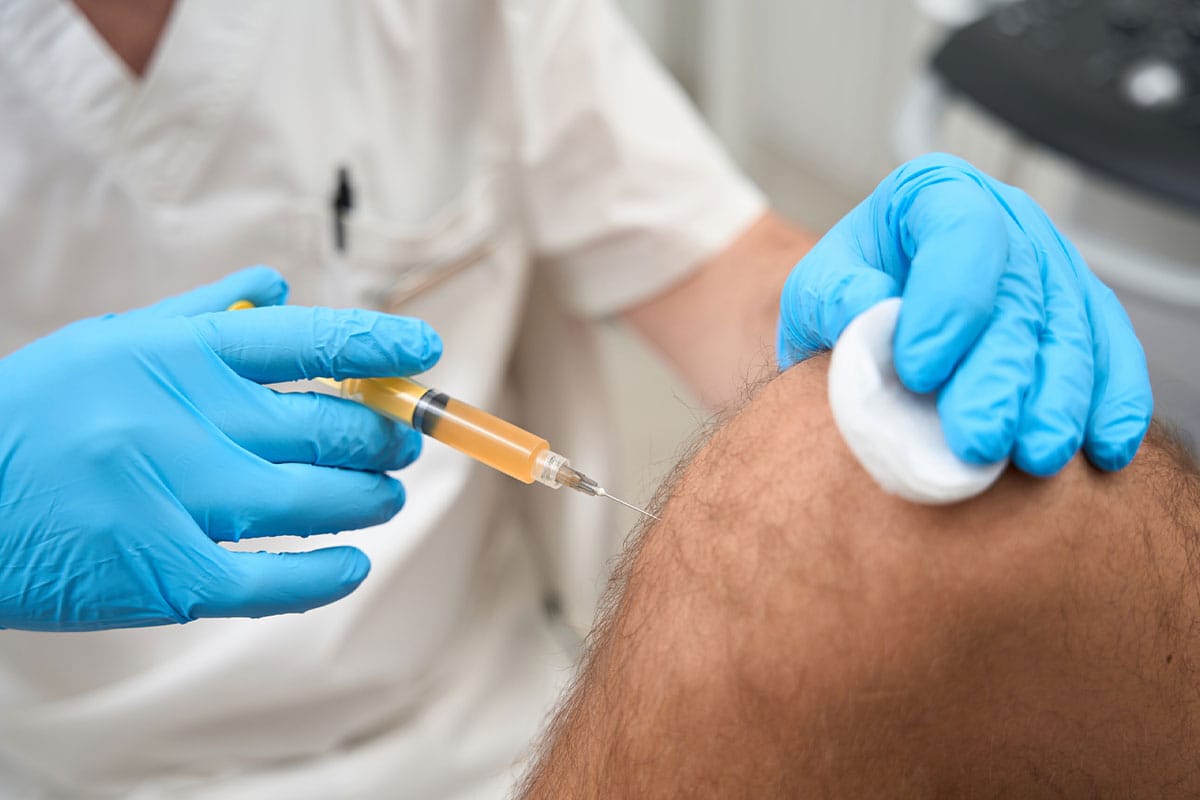 Gloved professional administering injection into patient’s knee.