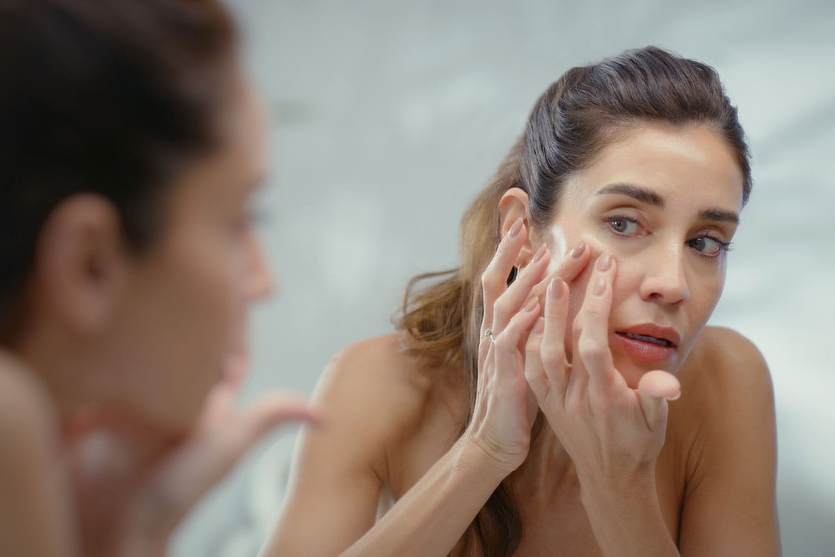 Woman examining facial skin in mirror.
